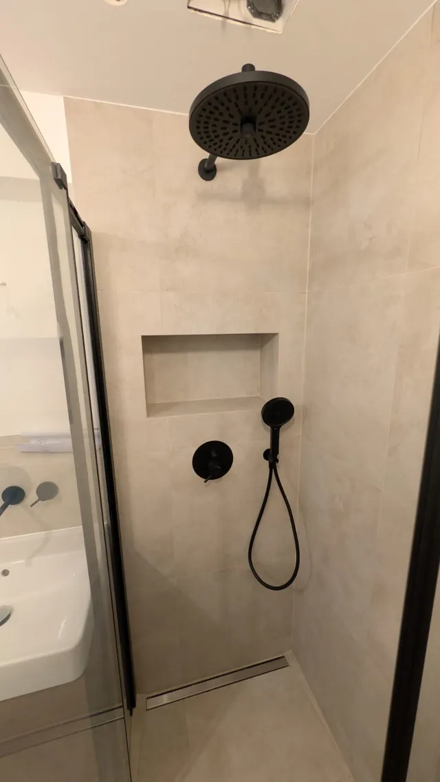 Walk-in-Dusche mit Regenbrause und schwarzen Armaturen in großformatigen Fliesen