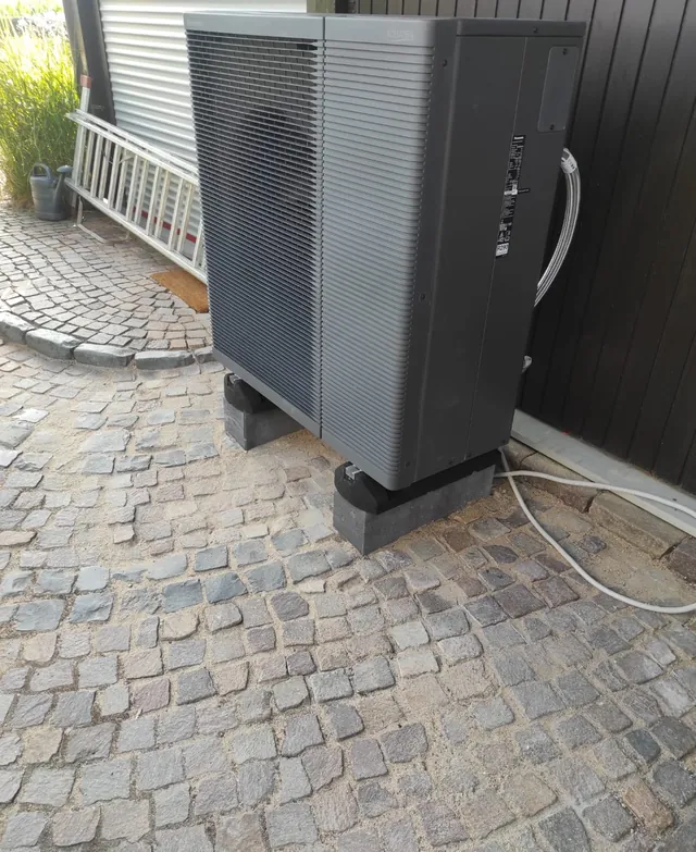 Außeneinheit einer Luft-Wasser-Wärmepumpe auf einer Pflasterfläche neben dem Haus